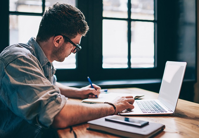 young man studying at a computer and taking notes